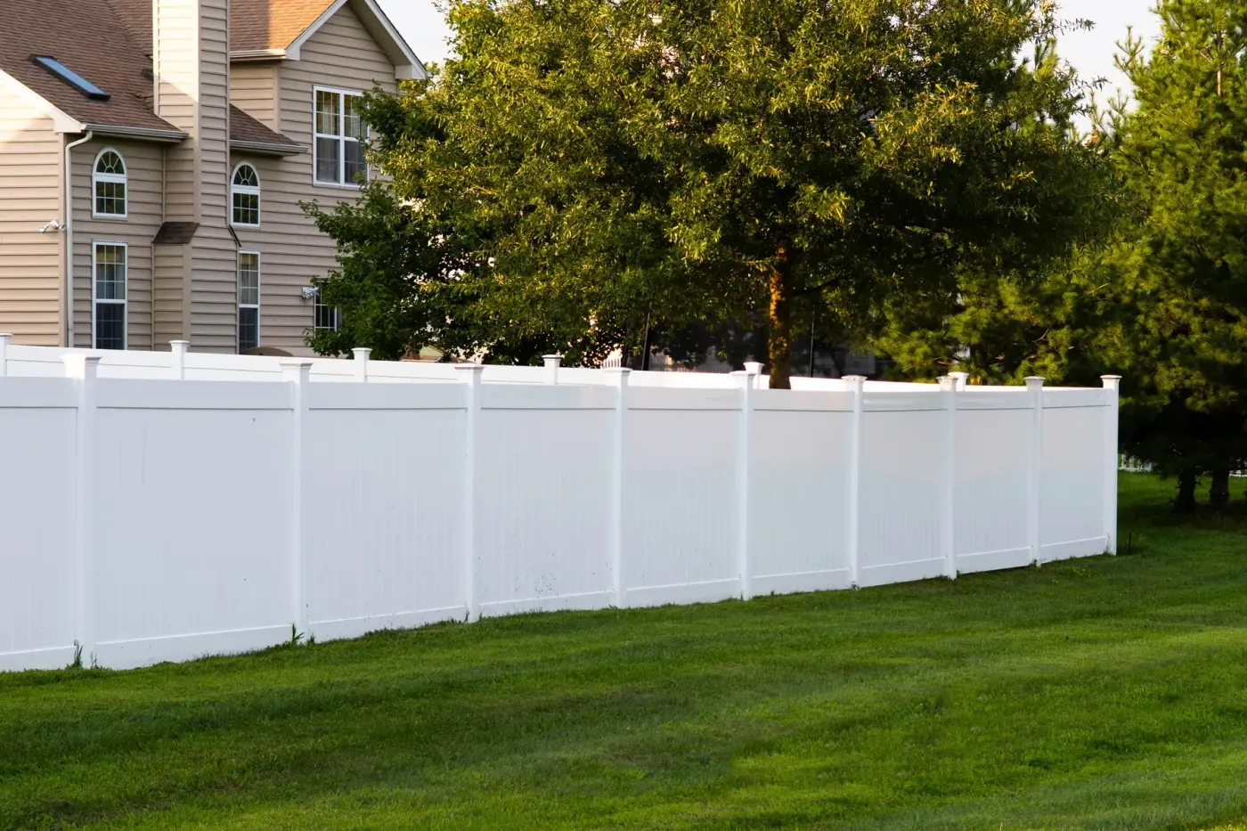 White vinyl privacy fence with flat post caps running along a mowed lawn beside a two-story house