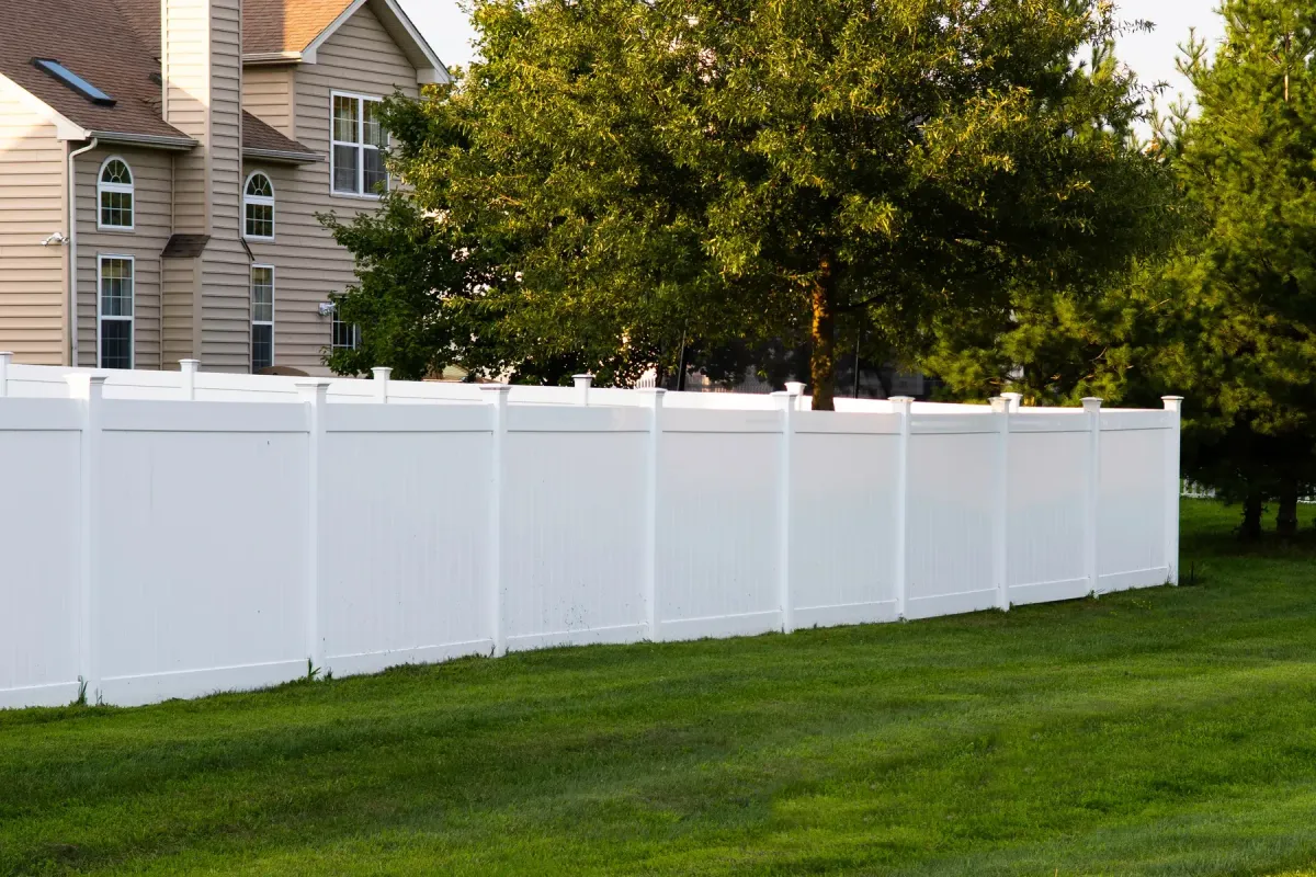 White vinyl privacy fence with flat post caps running along a mowed lawn beside a two-story house